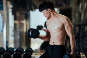 Athletic man performing dumbbell bicep curls during strength training workout in a gym, representing exercise and muscle preservation during tirzepatide weight loss therapy treatment.