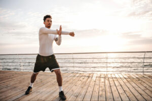 Active man stretching outdoors near the water during sunrise, representing healthy lifestyle habits, movement, and long-term wellness support through physician-guided care at IntegraMed Wellness in Boynton Beach, FL.